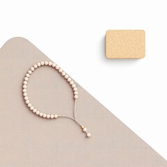 Overhead view of a delicate light pink beaded bracelet resting on a beige surface next to a small rectangular beige object, isolated on white background