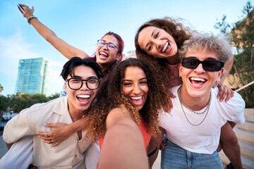 Five cheerful friends having fun, pose for a playful selfie in a bright urban city, sharing laughter and energy. Diverse young adults enjoying travel vibes and genuine connection outdoors.