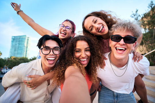 Five cheerful friends having fun, pose for a playful selfie in a bright urban city, sharing laughter and energy. Diverse young adults enjoying travel vibes and genuine connection outdoors.