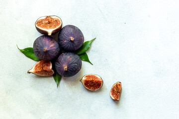 Purple ripe figs fruit and slices with green leaves top view on a stone background