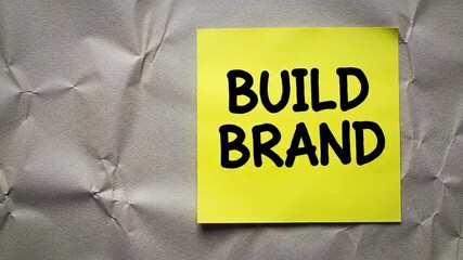 A Yellow sticky note with build brand text on a wrinkled gray background. Perfect for marketing and business concepts.  - Powered by Adobe