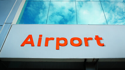 Fototapeta premium Prominent airport sign fixed on a modern terminal building, with vibrant cloud reflections dancing across the sleek glass facade, symbolizing travel, logistics, and global connection