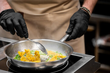 Chef cooking fresh yellow tortellini pasta with green peas and creamy white sauce in a stainless steel pan in a restaurant kitchen setting