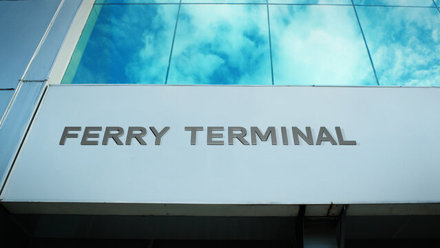 Ferry Terminal sign on a modern building with cloud reflections on glass windows, representing transportation services, urban architecture, and exterior concept