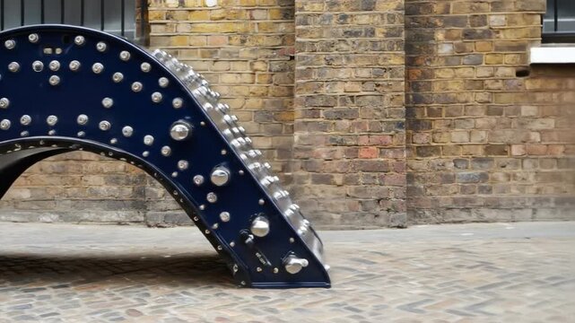 A dark blue metal archway sculpture studded with silver rivets, set against a brick wall background