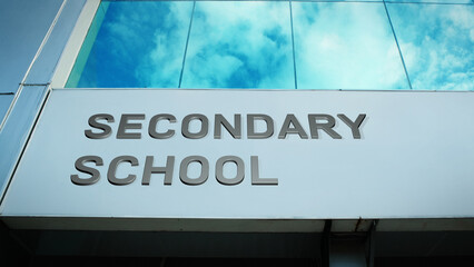 Secondary School sign displayed on a modern glass building with windows reflecting clouds and sky, creating a clean, bright, contemporary exterior with educational atmosphere