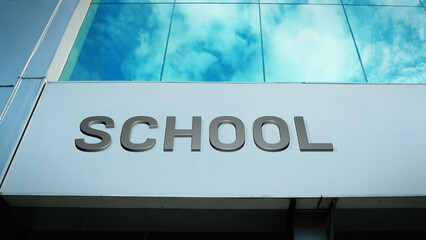 School sign displayed on a modern glass building with windows reflecting clouds and sky, creating a clean, bright, contemporary exterior with educational atmosphere