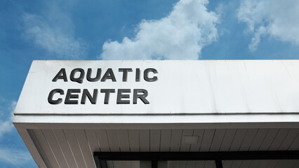 Aquatic Center word sign displayed on building facade under blue sky, representing a facility for swimming, water sports, fitness, and recreational activities