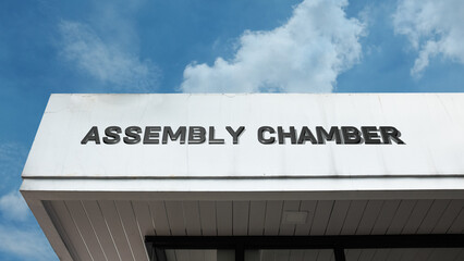 Naklejka premium Assembly Chamber word sign displayed on building under clear blue sky, representing governance, meetings, legislation, and official public institutions