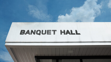 Banquet Hall word sign displayed on building under clear blue sky, representing events, celebrations, gatherings, and formal indoor venues © Herman