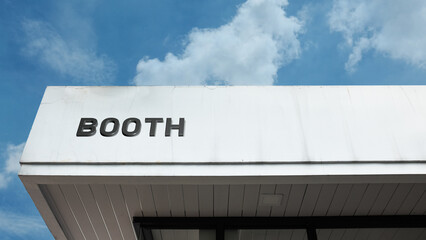 Booth word sign displayed on building under clear blue sky, representing small retail space, exhibition, kiosk, or temporary commercial structure