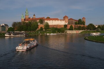 Historic Wawel Castle complex and Vistula River with cruise ship in foreground in afternoon sunlight. Krakow, Poland