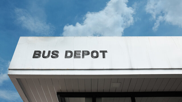 A bus depot word sign mounted on a building facade under a clear blue sky, with bold lettering and a clean exterior captured in bright daylight