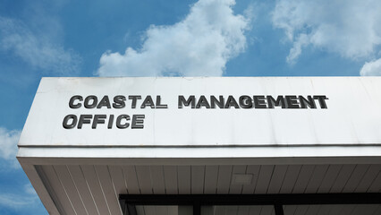 Obraz premium Coastal Management Office word sign displayed on a building under a clear blue sky, representing environmental oversight, shoreline protection, government services, and administration