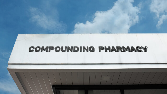 Compounding Pharmacy word sign displayed on a building under a clear blue sky, representing personalized medicine, pharmaceutical services, healthcare, and drug preparation