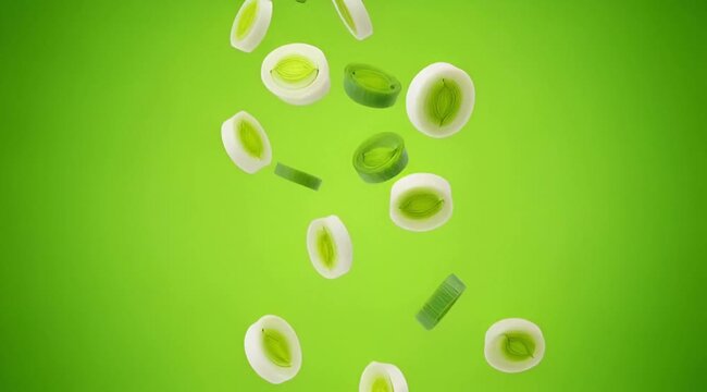 Sliced leeks or spring onions falling against a vibrant green background, showcasing fresh vegetables.