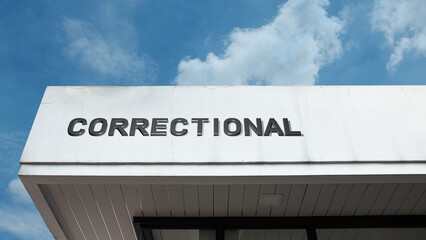 Correctional word sign displayed on a building under a clear blue sky, representing law enforcement, security, rehabilitation, prison management, and public safety