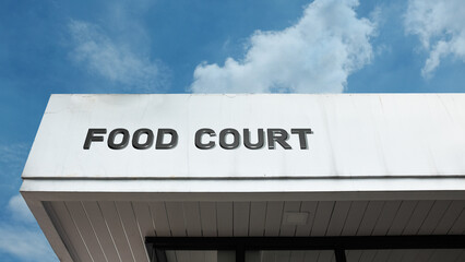 Obraz premium Food court word sign displayed on a building with a blue sky background, representing dining areas, eateries, and shared food service spaces