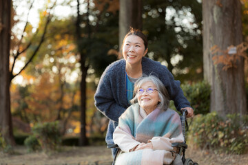 An elderly woman in a wheelchair taking a stroll amid the beautiful autumn foliage, accompanied by...