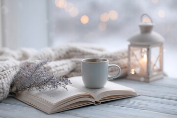 Cup of coffee and open book by candlelight in winter setting