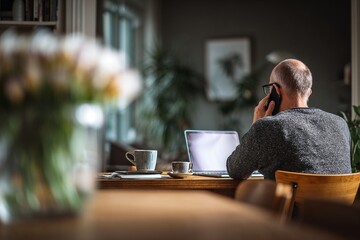 Middle-aged man working from home on phone with laptop