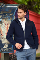 A man in a navy hoodie poses in front of an abstract painted wall. The artistic background adds a creative touch to this clean, casual portrait.