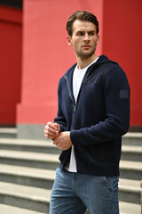 Close-up portrait of a man in a navy hoodie against a red wall. Clean minimalism and a confident, calm expression emphasize the contemporary casual look.