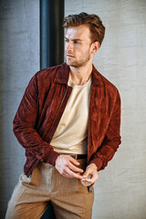 A man in a fitted green T-shirt sits casually on a chair, leaning back with relaxed confidence. The minimal background and soft shadows emphasize his physique and clean modern styling.