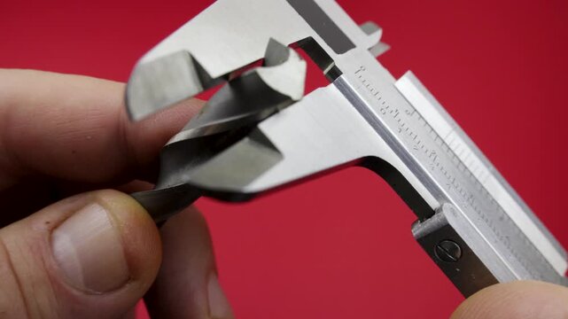 Drill bit measuring using caliper Woodworking Red background Hand holding a drill bit caliper measures its diameter vibrant red background. The caliper, a steel precision instrument DIY and workshop