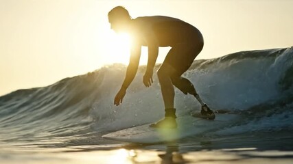 Adaptive surfer with a prosthetic leg riding a wave at sunset. Slow motion.