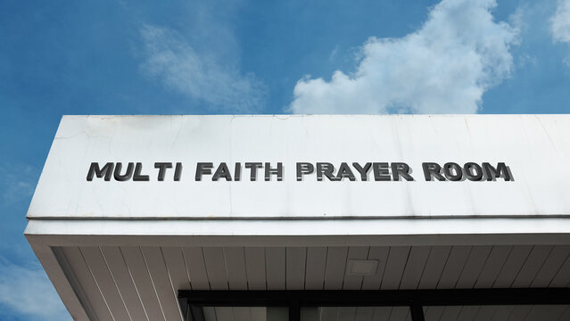 Multi-Faith Prayer Room sign on a building against a clear blue sky, symbolizing interfaith harmony, spiritual inclusion, communal worship, meditation, universal devotion, and tolerance