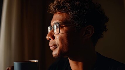A man enjoys a quiet morning with a warm cup of coffee while gazing out at the city skyline. The sunlight creates a serene atmosphere in his room