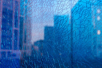 Obraz premium Blue shattered glass reflecting apartment windows, with cracks suggesting violence, danger, and crime, creating a tense and unsettling urban scene