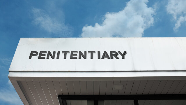 Penitentiary word signage on a massive institutional building under a blue sky, symbolizing incarceration, law enforcement, corrections, and justice system