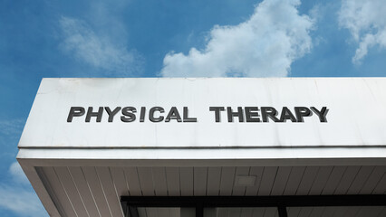 Obraz premium Physical Therapy word signage on a healthcare building under a blue sky, symbolizing rehabilitation, medical treatment, wellness, and professional recovery services