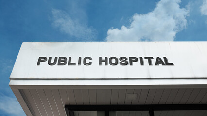 Obraz premium Public Hospital word signage on a medical building under a blue sky, symbolizing healthcare, government service, medicine, emergency care, and community wellness.