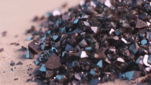 A close-up view presents a pile of sparkling, dark, fractured fragments on a textured surface