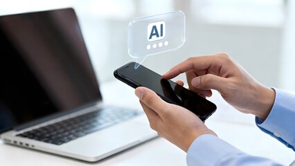 Hands holding a smartphone with an AI chat bubble using artificial intelligence on a mobile device with a laptop in the background