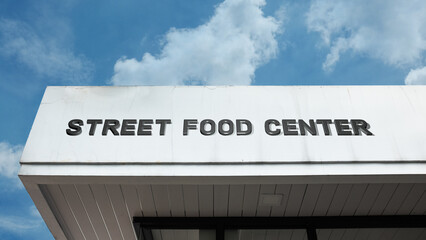 Fototapeta premium Street Food Center word signage on a commercial or public building under a blue sky, symbolizing eating, culinary culture, vendor hub, quick meals, tourism, dining, and diverse cuisine