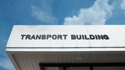 Obraz premium Transport Building word signage on a facility building under a blue sky, symbolizing logistics, public transit, travel, infrastructure, movement, mobility, and transportation hub