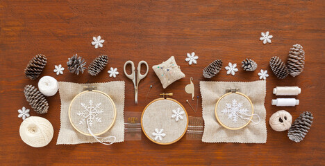 Making handmade Christmas gifts. Embroidered snowflakes on canvas in a hoop and craft accessories on a wooden table. Preparing for Christmas holidays. Flat lay, close-up, copy space, top view