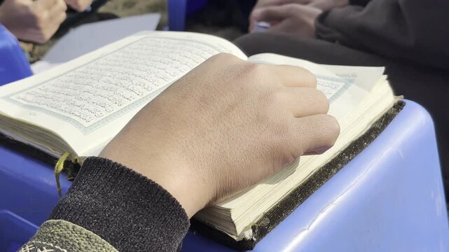 Closeup shot of a muslim boy reading holy Quran in the month of Ramadan. A little muslim student reciting holy book Quran and islamic holy book. Muslim boys reading holy Quran during pray and fast.