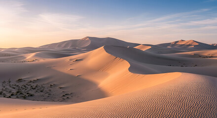 Expansive view of sand dunes under a clear sky at sunset in a desert landscape with ripples and shadows