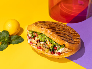 Tasty chicken shawarma with vegetables, lemon and sauce in a pita bread on bright yellow and purple background. Colorful food photography, bright color food image.