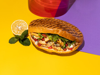 Tasty chicken shawarma with vegetables, lemon and sauce in a pita bread on bright yellow and purple background. Colorful food photography, bright color food image.