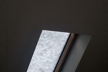 Interior view of a slanted skylight window blocked by snow, diffusing light into a dark room and creating a cold winter mood.