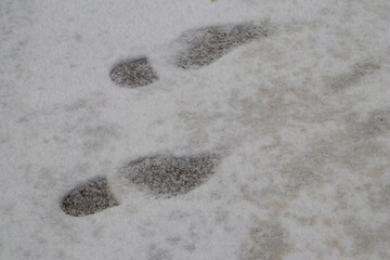 Detailed view of human shoe prints left in soft, slightly dirty snow, showing clear impressions during a cold winter day.