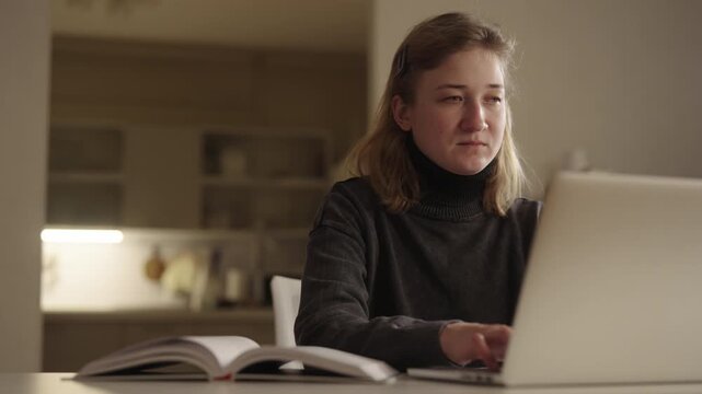 Exhausted young woman with cerebral palsy struggling to stay awake while studying late at night, eventually falling asleep in front of laptop and book in dimly lit home environment, slow motion.