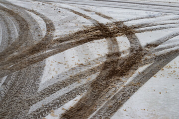 Multiple vehicle tire tracks forming intersecting patterns on a slushy and dirty snow-covered road during winter weather conditions.