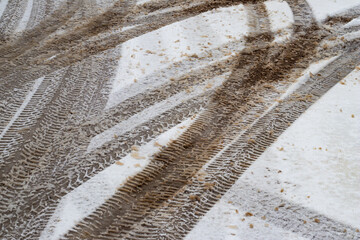 Multiple vehicle tire tracks forming intersecting patterns on a slushy and dirty snow-covered road during winter weather conditions.